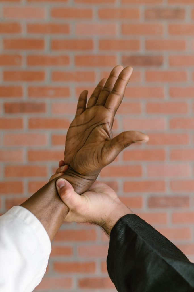 Close-up of martial arts hand training with two people against a brick wall background.
